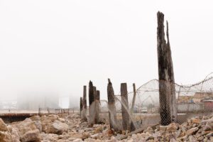 Forgotten wasteland: weathered wooden posts, rocky terrain, distant structures in fog.