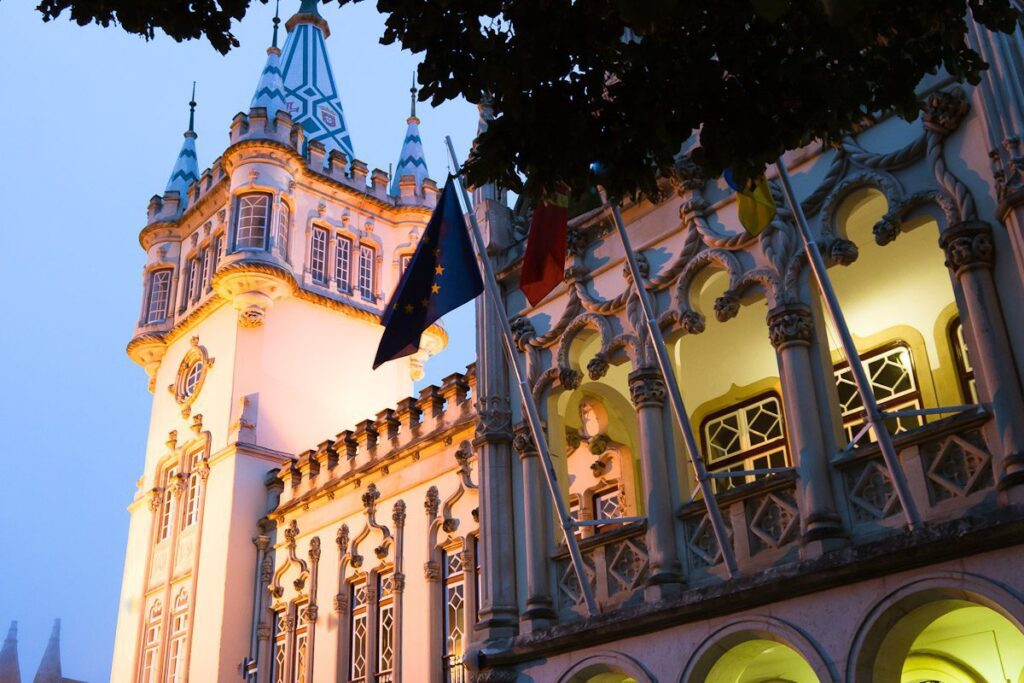 Twilight Gothic architecture illuminated by warm light and colorful flags at dusk.