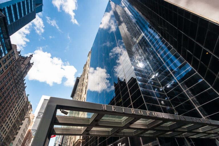 Modern glass skyscraper reflecting blue sky next to historic stone building in vibrant cityscape.