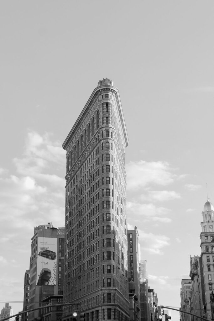 Iconic Flatiron Building in NYC: Triangular form in black and white against urban backdrop.