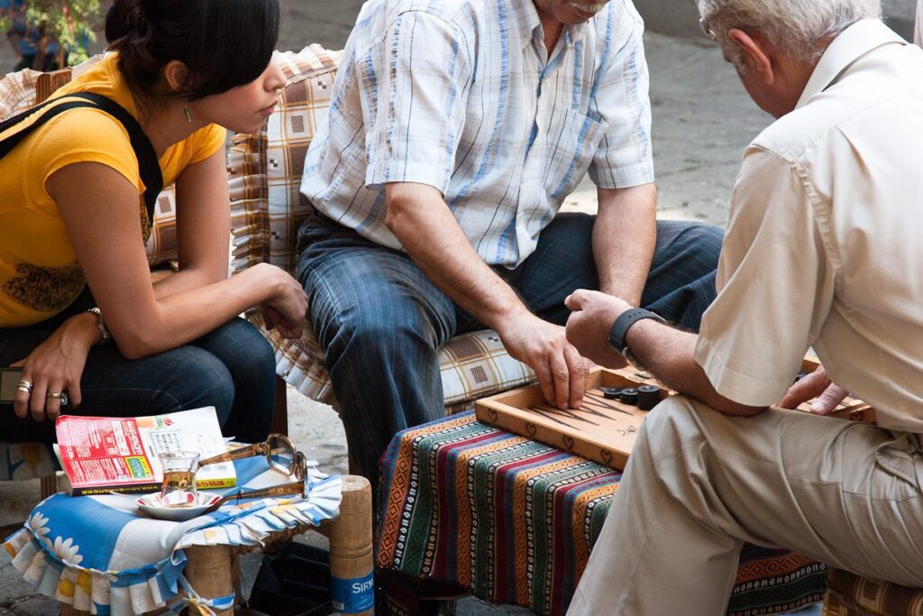 Friends playing outdoor backgammon, engrossed in colorful game on a vibrant table.