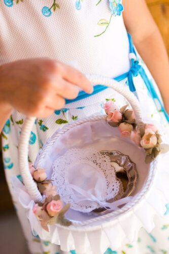 Elegant wedding basket with pink roses, held by person in blue floral dress.