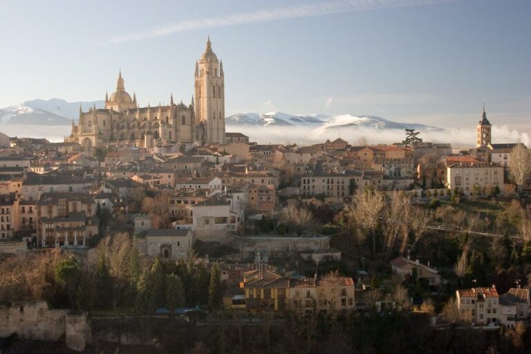 Golden hour in a historic European city with a grand Gothic cathedral and snow-capped mountains.
