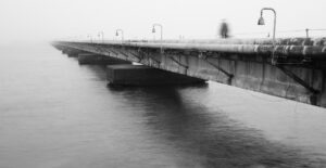 Misty bridge crossing with solitary figure disappearing into fog, evoking solitude and mystery.