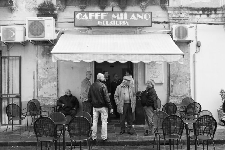 Charming café scene: locals chatting outside Caffé Milano Gelateria in black and white photo.