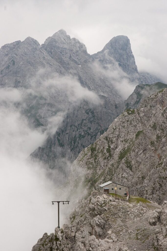 Majestic mountain landscape with mist-shrouded peaks, rugged cliffs, isolated refuge, and utility pole.