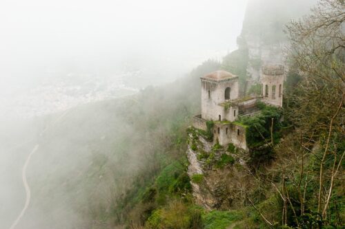 Enchanting castle ruins in misty hillside with stone walls, towers, and overgrown vegetation.