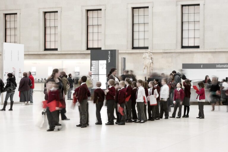 Schoolchildren exploring museum art with guide and visitors in spacious, serene environment.