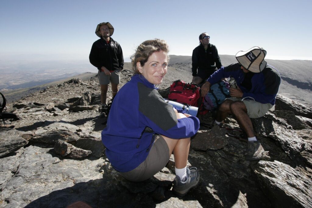 Four hikers on a rocky summit, enjoying panoramic mountain views.