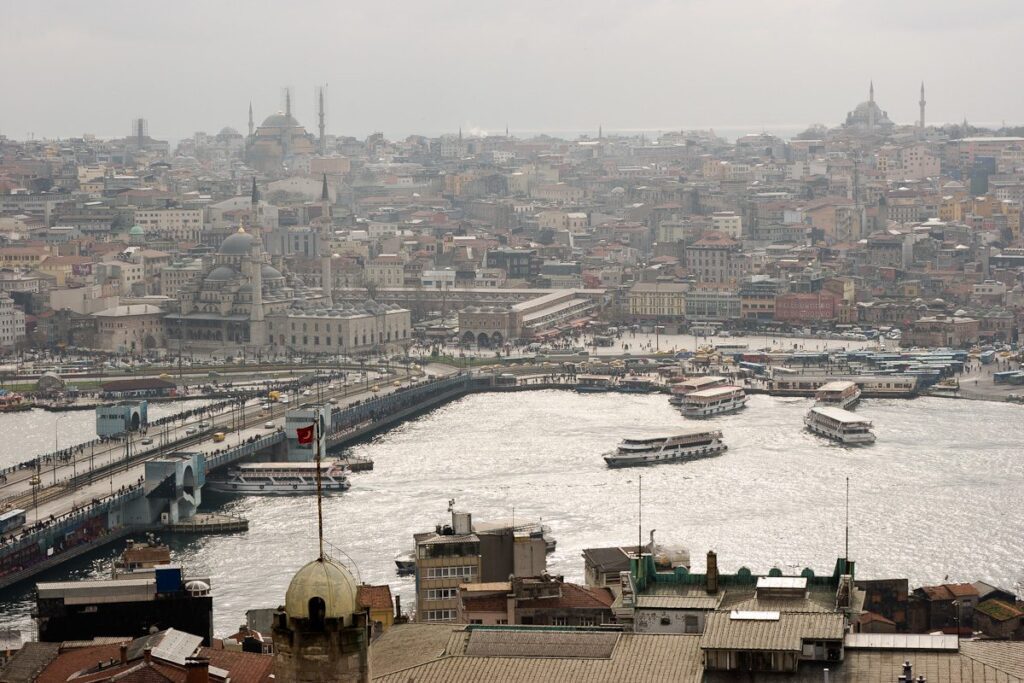 Tranquil cityscape with bridge, boats, historical buildings, and cultural landmarks in a hazy urban setting.