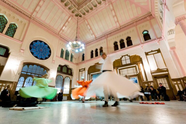 Sufi dancers whirl gracefully in ornate hall, captivating audience with spiritual performance.